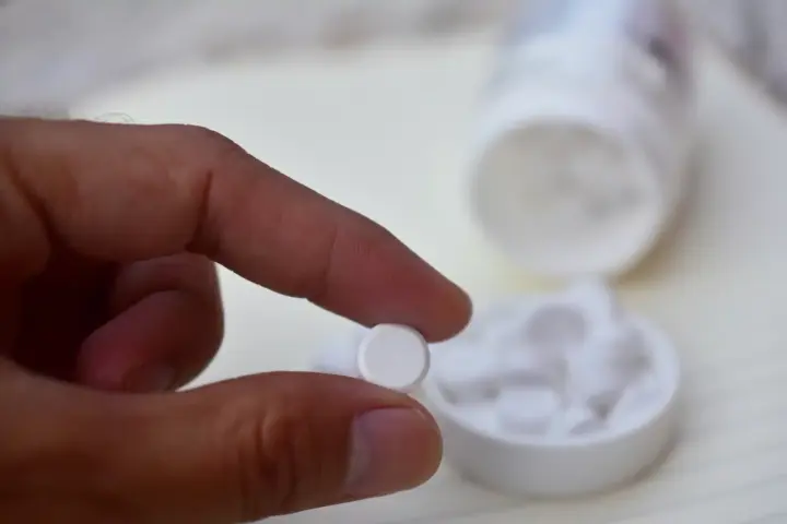 How Long Does Buprenorphine Stay In Your System? A person using two fingers to pick up a round white pill.