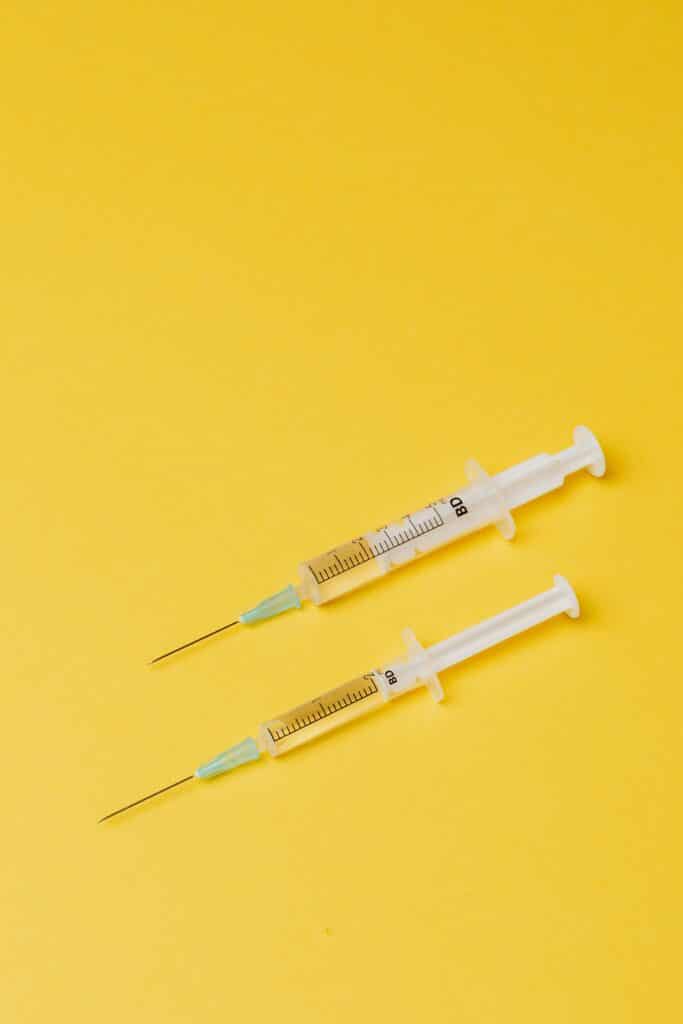 Two medical syringes filled with liquid placed on a bright yellow background.