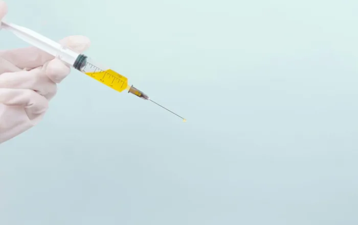 A hand wearing a white glove holding a syringe filled with an unidentified substance, possibly linked to the question, “Can you overdose on ketamine?”