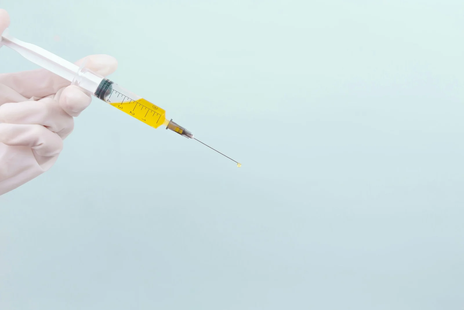 A hand wearing a white glove holding a syringe filled with an unidentified substance, possibly linked to the question, “Can you overdose on ketamine?”