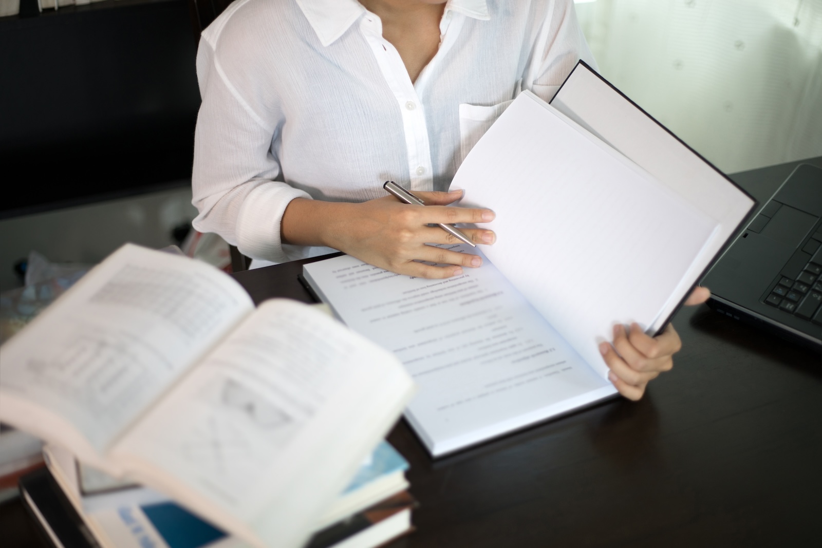 woman reading a book at her desk with stack of other books next to her