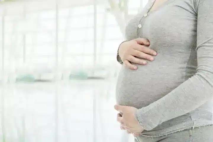 Can You Take Adderall While Pregnant: A pregnant woman cradling her stomach in front of a window.