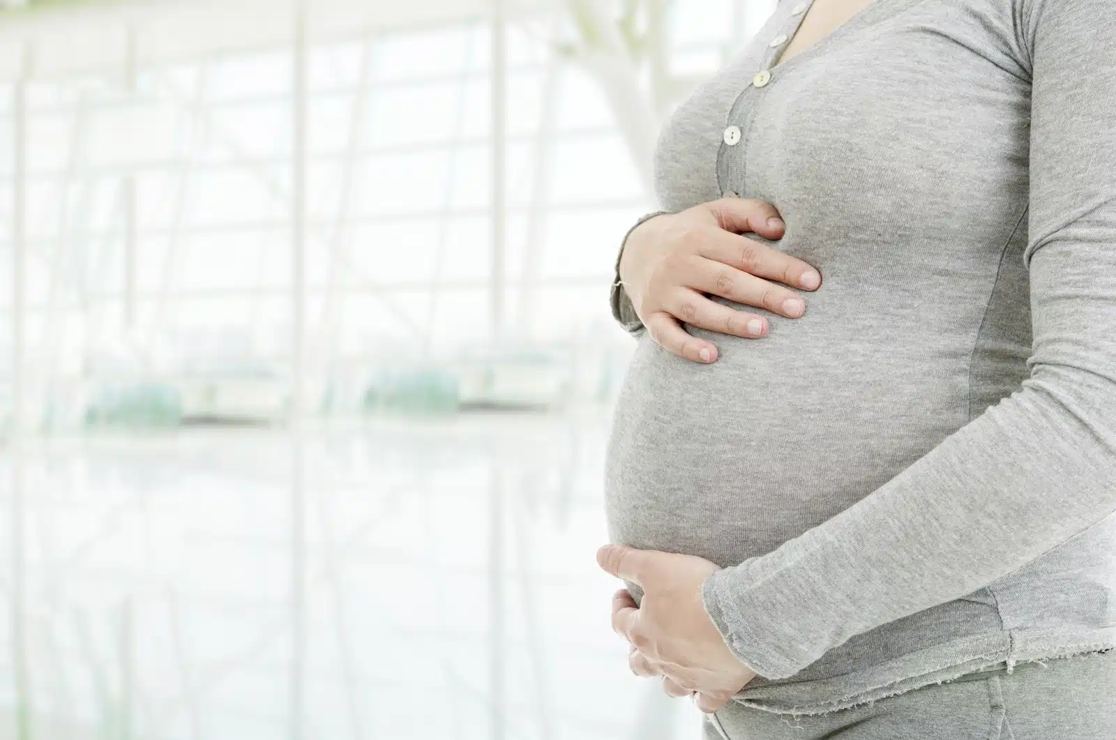 Can You Take Adderall While Pregnant: A pregnant woman cradling her stomach in front of a window.
