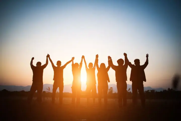The AA Prayer: A group of people with their hands held in the air during sunset.