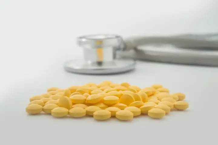 Is Cyclobenzaprine A Controlled Substance? A pile of small round yellow pills on a white surface with a stethoscope in the background.