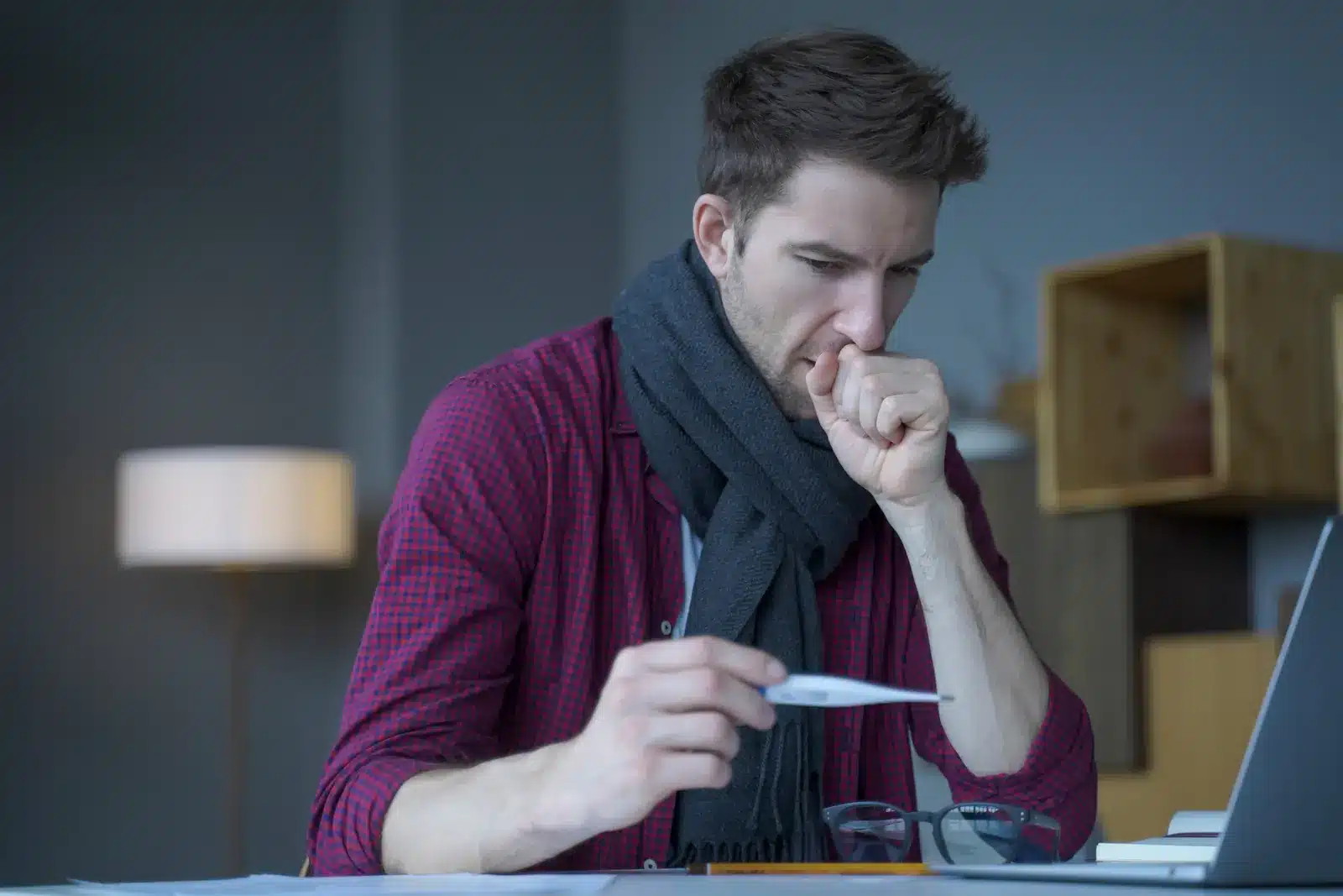 Can you overdose on cough drops. Male in scarf around his neck coughing looks at digital thermometer